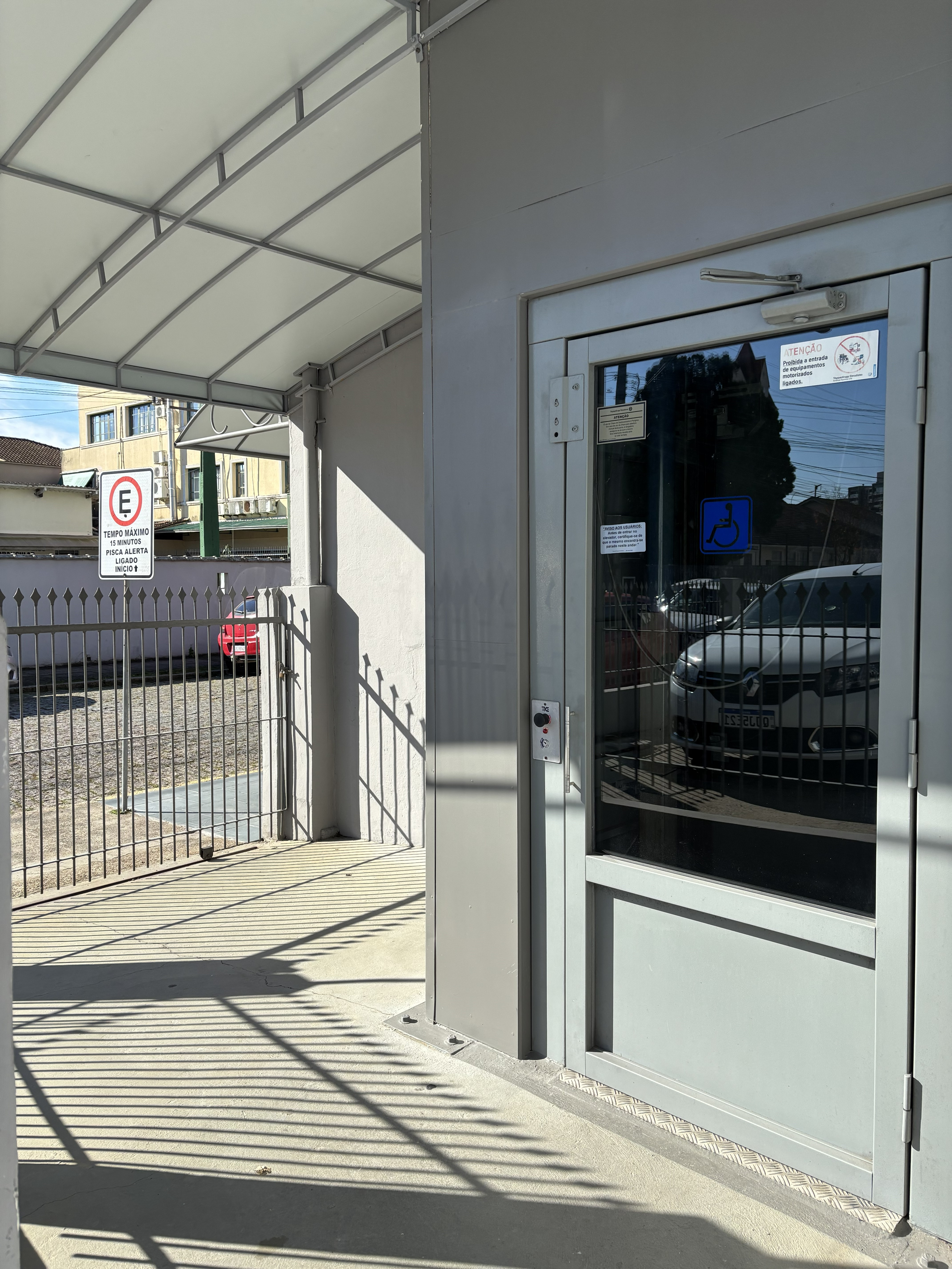 Entrada coberta do elevador com porta de vidro larga e símbolo internacional de acessibilidade